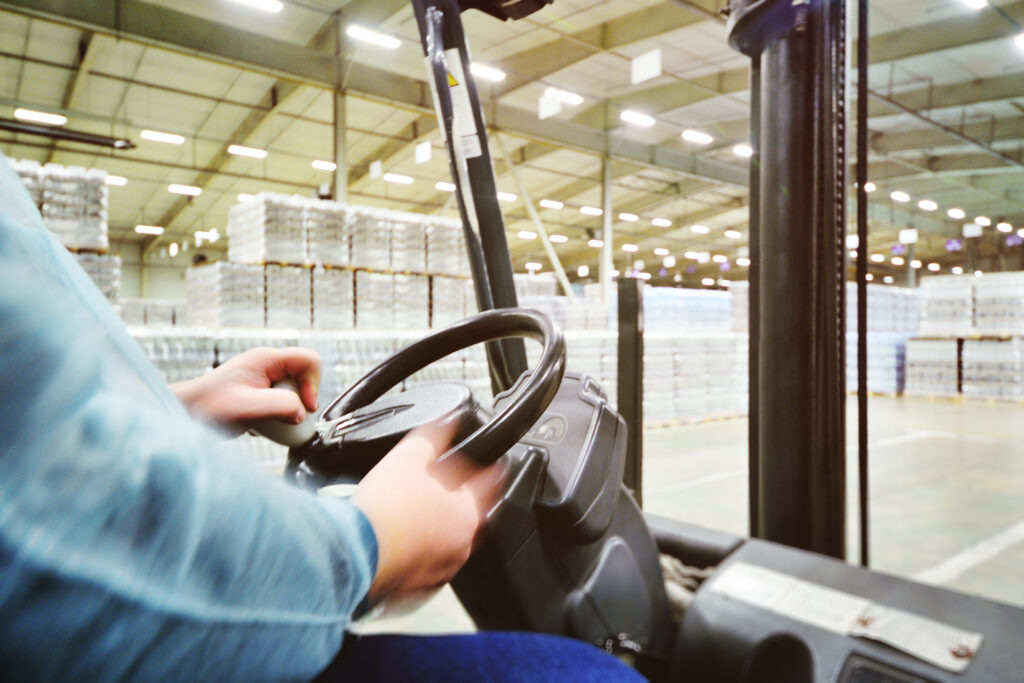 Hands Of A Warehouse Worker Who Operates A Forklift Against The Background Of Tetra Packs With Drinks, Water, Beer.
