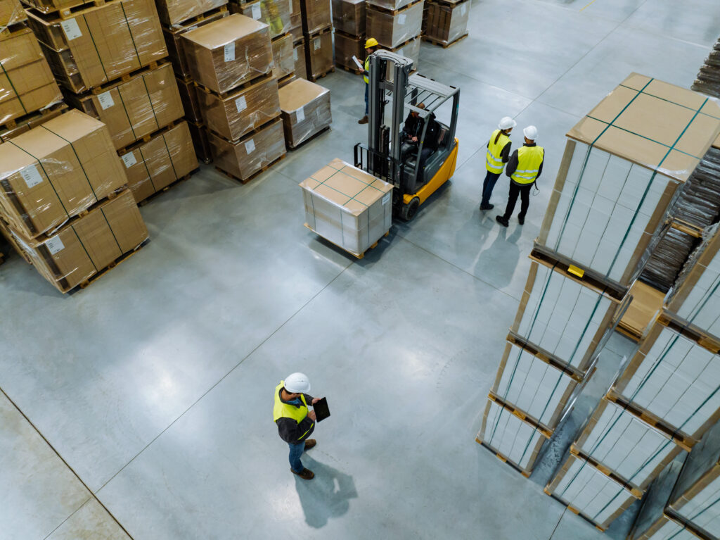 Top View Of Workers Modern Warehouse Storage Of Retail Shop, Large Factory Workshop Space. Employees In Modern Industrial Factory With Warehouse.