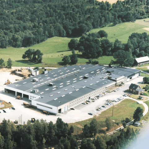 An older aerial view of the Troax facility nestled in a lush green landscape.